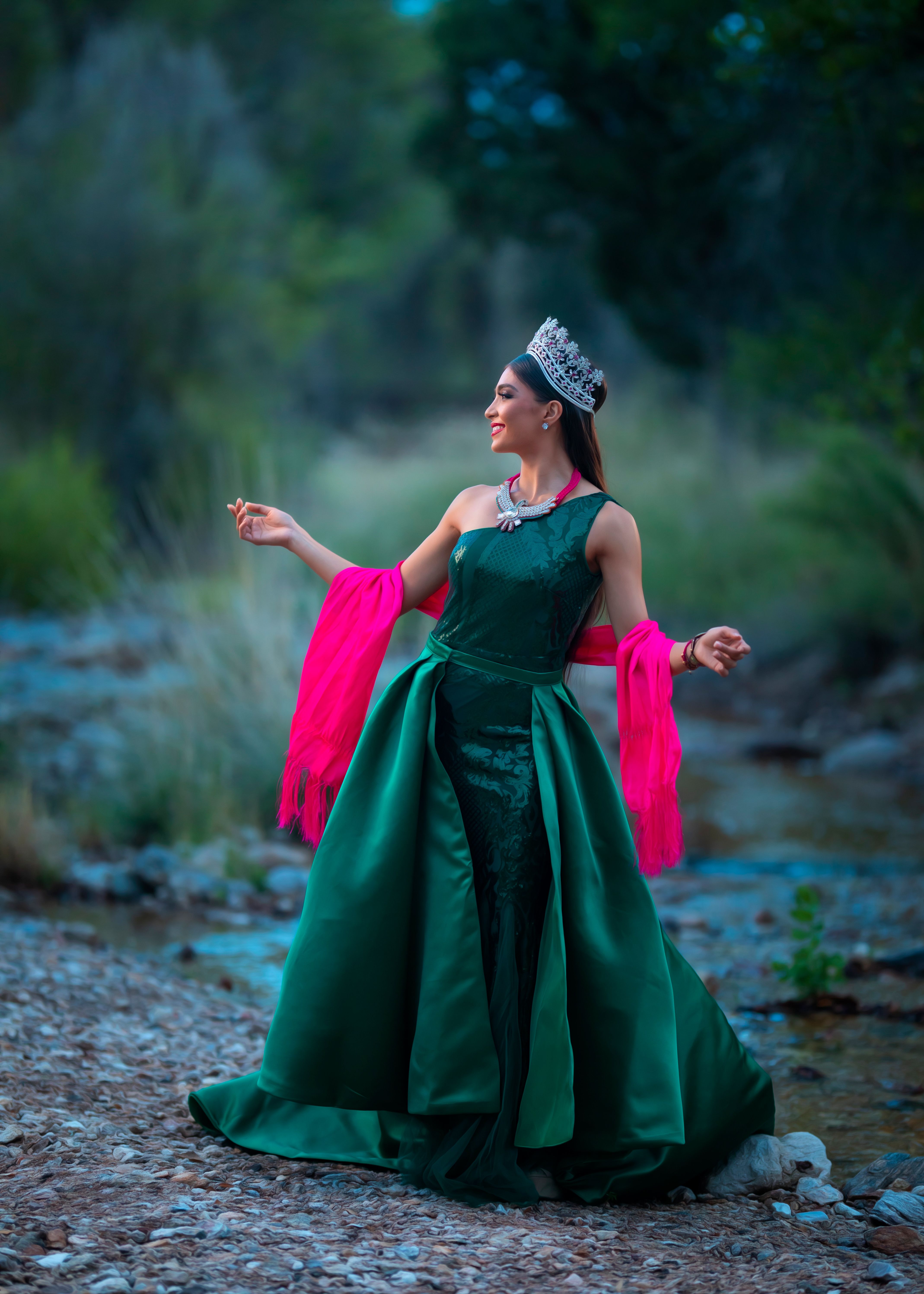 Elegantly dressed woman in a green gown and tiara standing outdoors. Captured with artistic beauty.