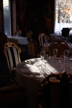 Sunlight filters through a classy restaurant's windows, illuminating table settings and ornate chairs.
