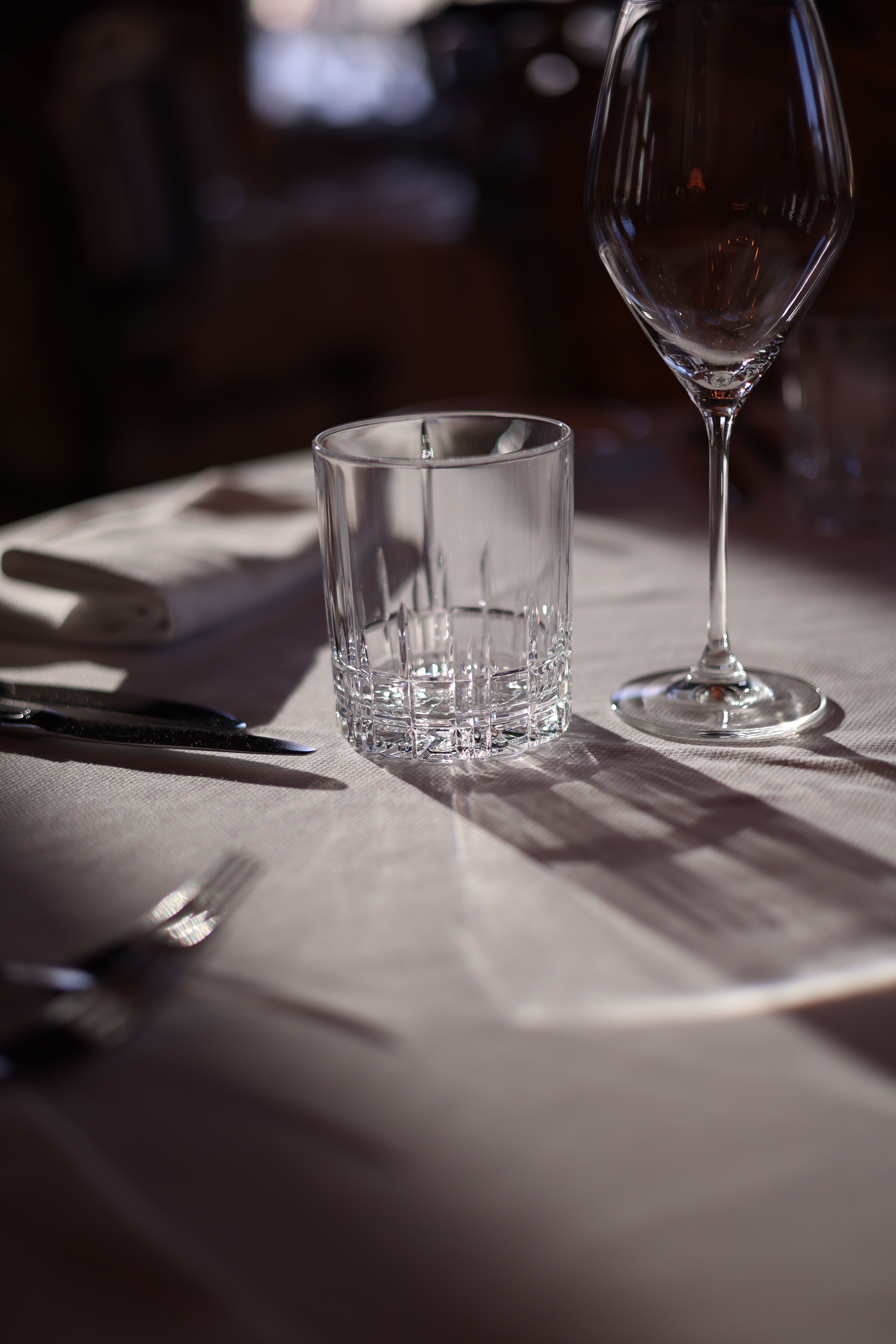 A refined table setting featuring glassware under warm lighting, creating elegant shadows.