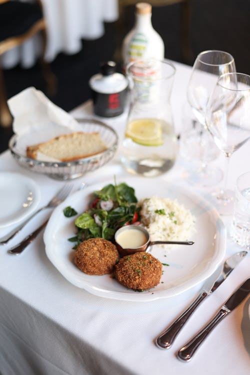 Free Close-up of gourmet crab cakes with salad on a white tablecloth, elegant dining setting. Stock Photo
