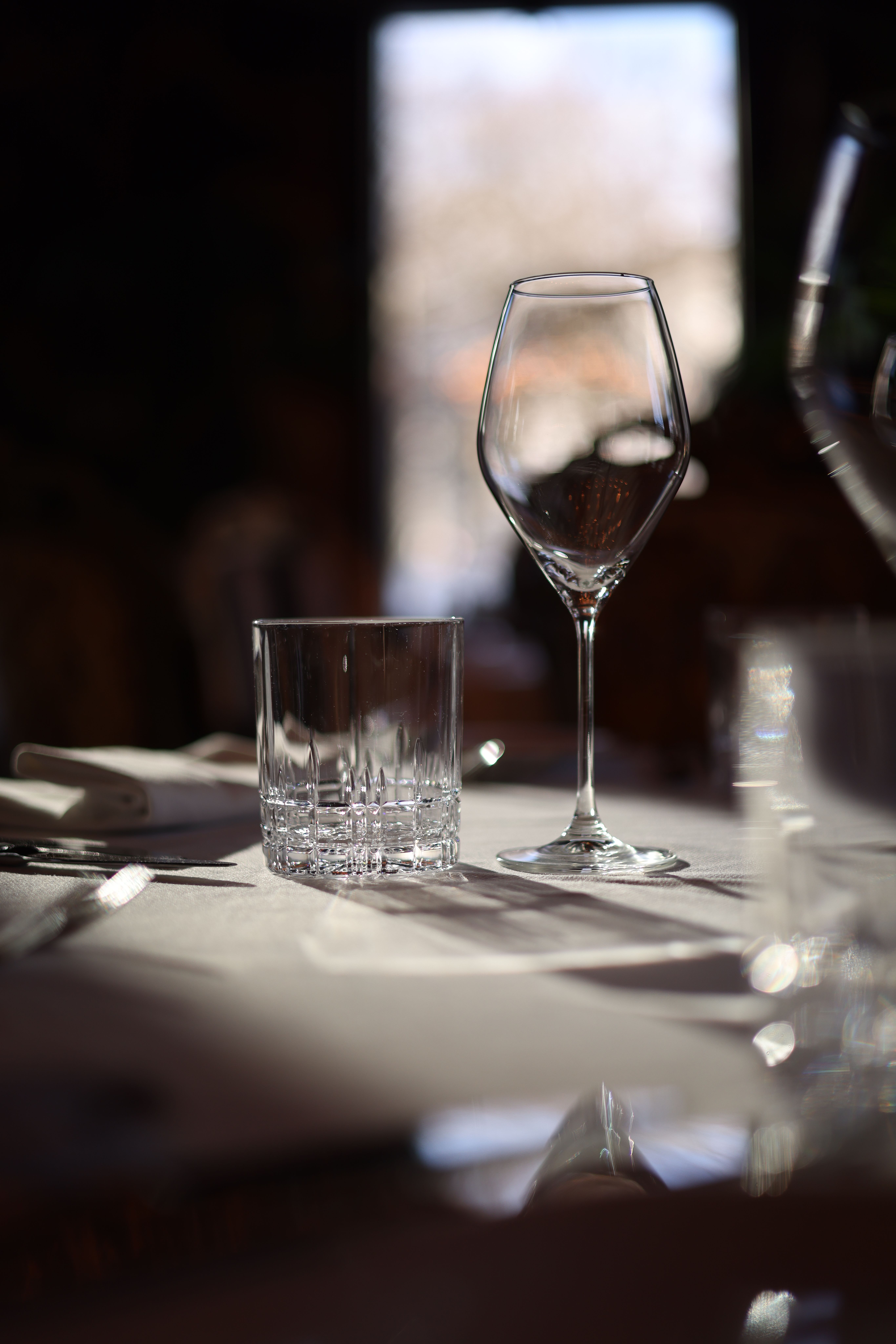 A close-up shot of a wineglass and highball glass on a sunlit table, perfect for dining themes.