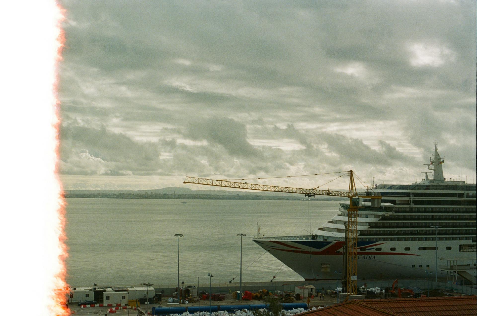 Large cruise ship docked in a harbor under overcast skies with construction crane visible.