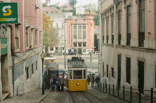 A yellow tram is traveling down a narrow street