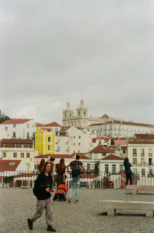 A group of people walking in a city with a large building in the background