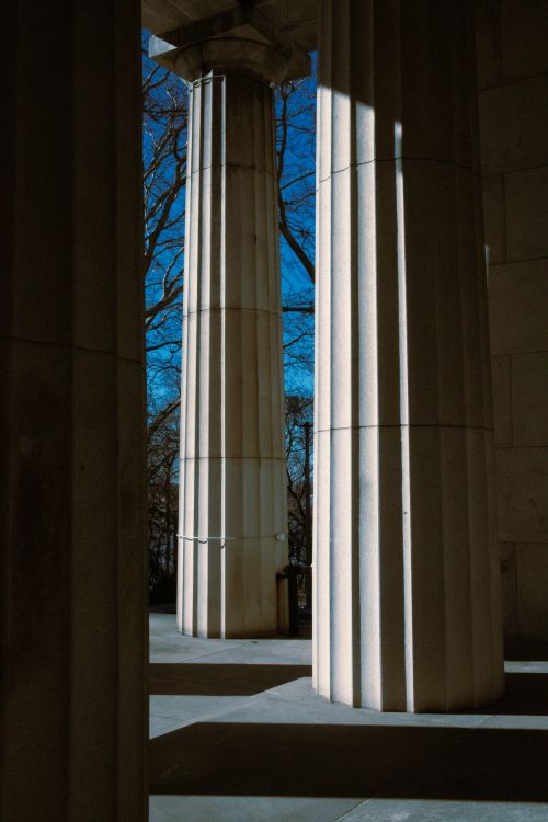 Free Elegant marble columns with striking sunlight and shadows in a classical outdoor setting. Stock Photo