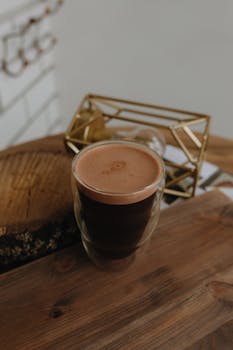 A freshly brewed coffee in a double wall glass on a rustic wooden table indoors.