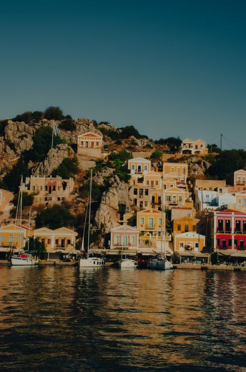 Free Vibrant houses line the seashore of Symi Island, Greece, reflecting in calm waters. Stock Photo