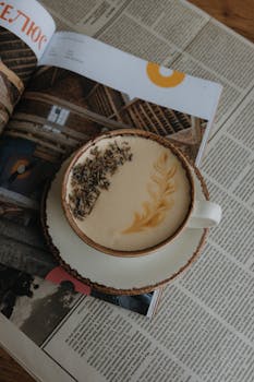 A beautifully crafted latte with artistic foam sits atop a magazine, perfect for a relaxed coffee moment.