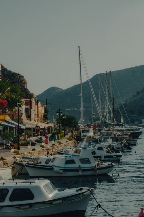Free Charming Greek marina scene with boats docked by a quaint village and mountains. Stock Photo