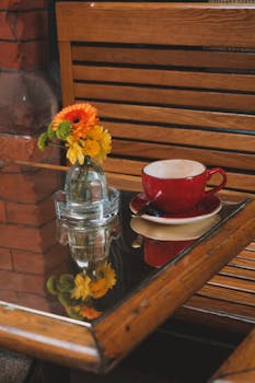Warm café setting with a red coffee cup and fresh flowers on a wooden table.