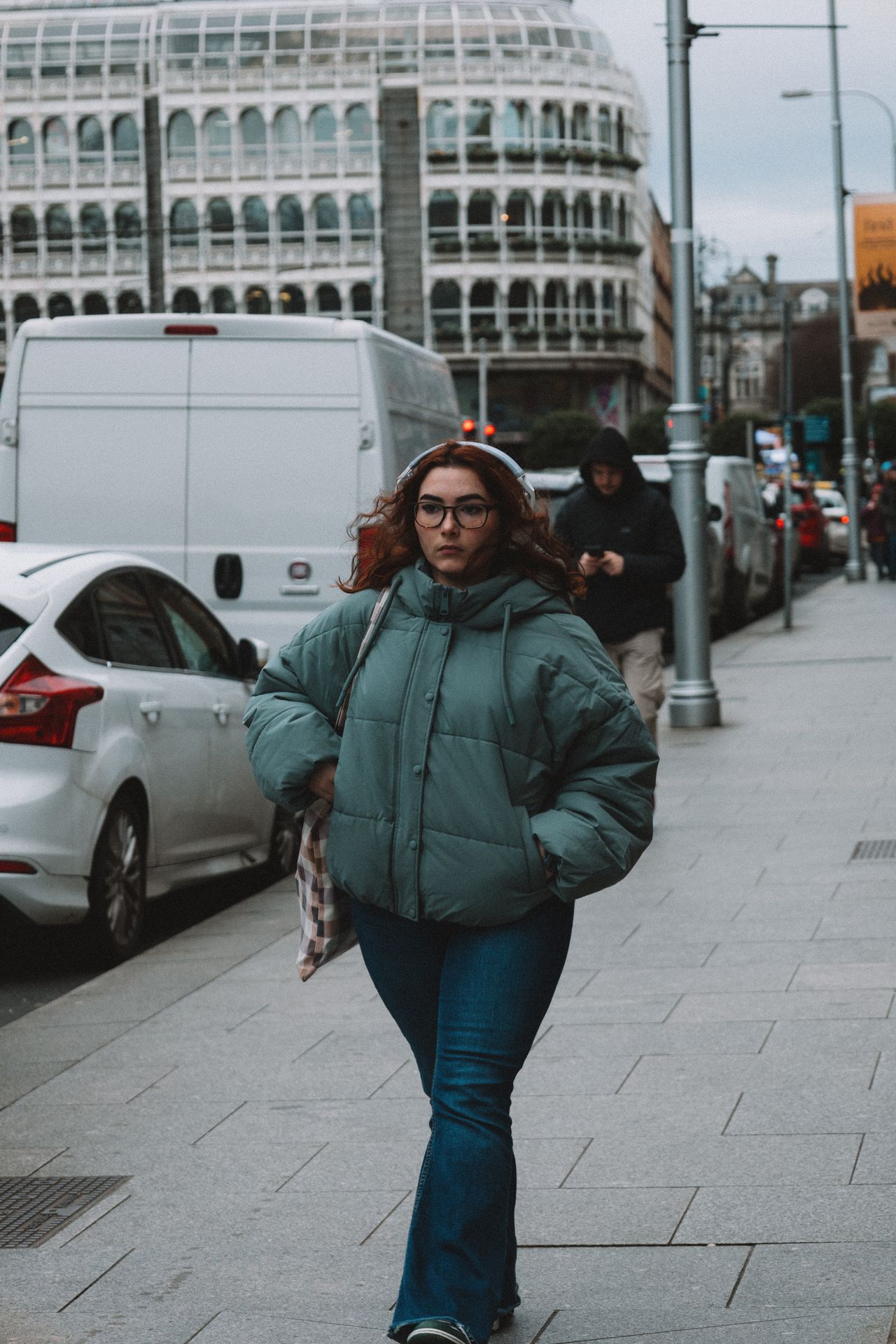 Woman in a sage green puffer jacket and jeans walking on a city sidewalk