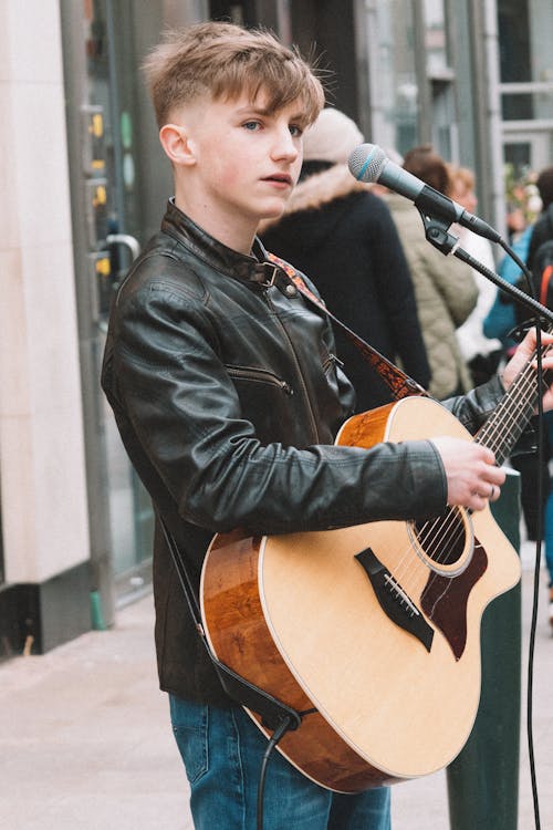 A young man is playing an acoustic guitar on a street