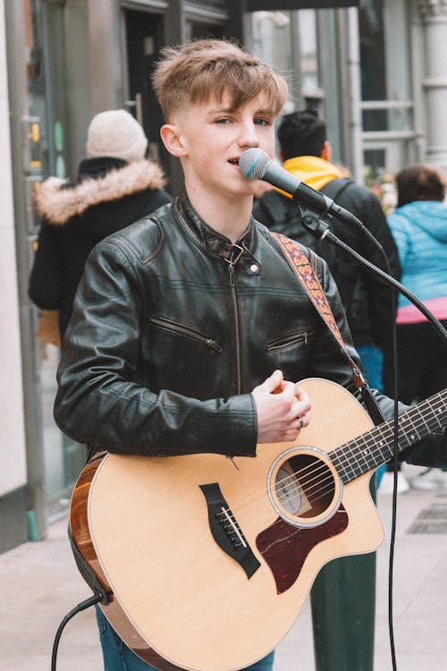 A young man with a guitar and microphone on a street