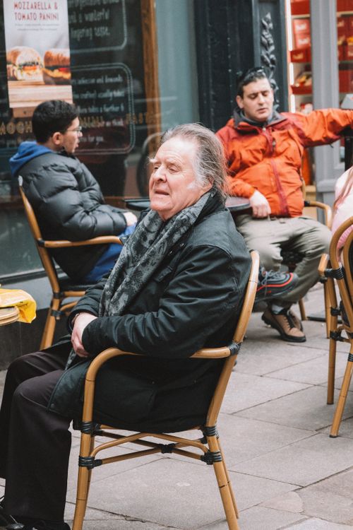 Free Elderly man sitting at a café outdoors, enjoying an urban setting. Stock Photo