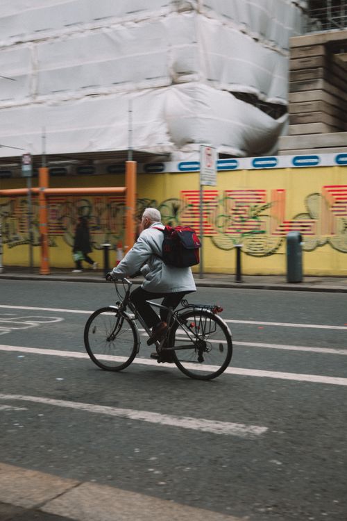 Free Senior man cycling on a city street with graffiti walls in an urban setting. Stock Photo