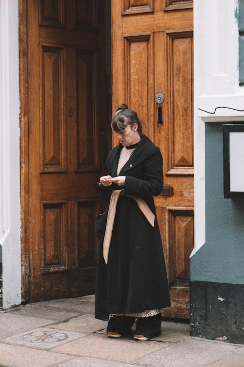 Woman in Black Coat Standing by Large Wooden Doors
