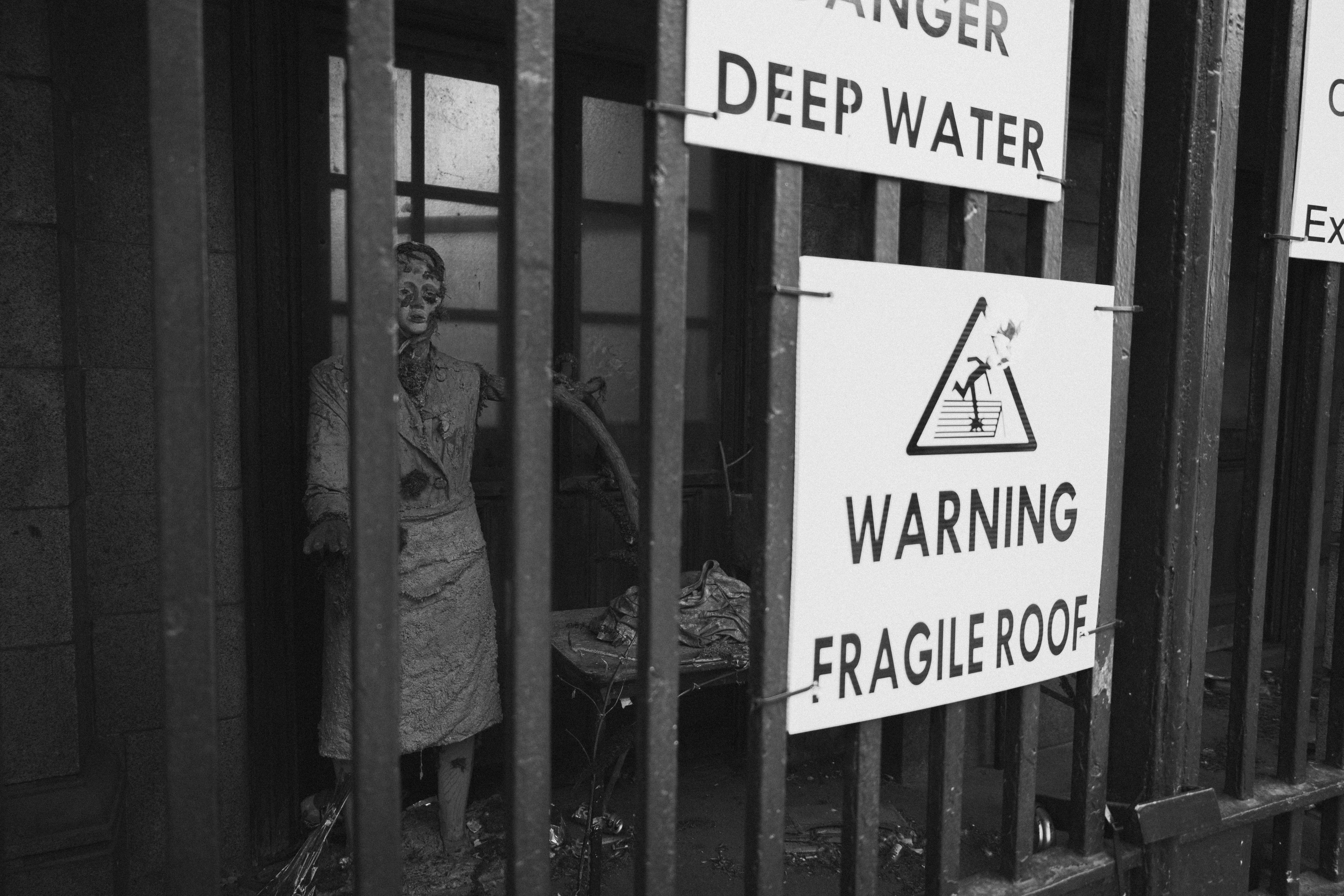 Eerie scene of a mannequin behind bars with warning signs indicating danger.