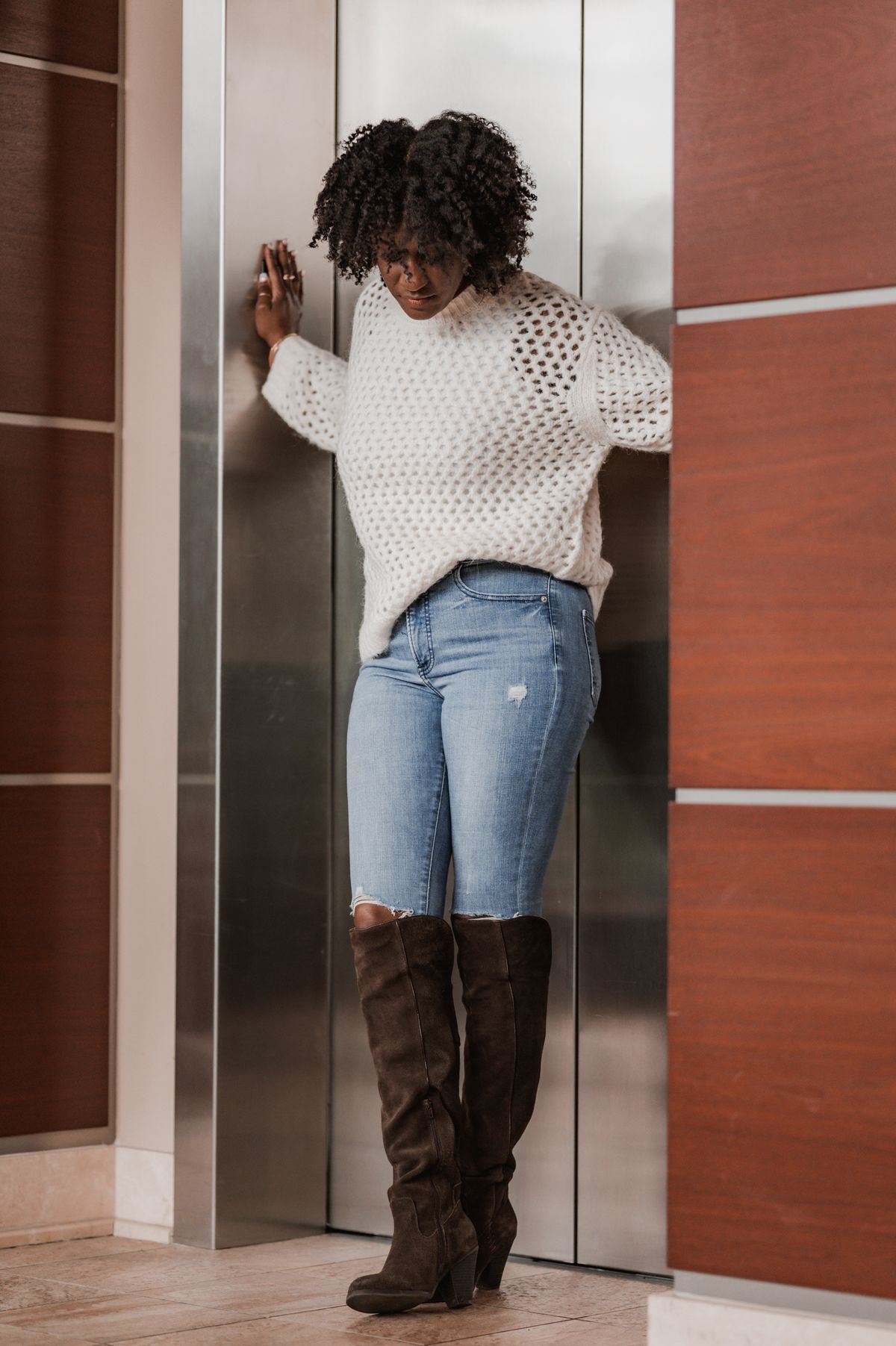 Fashionable woman in a white sweater and boots standing in an elevator.