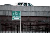 A bike route sign directing cyclists amidst urban traffic on an overpass.