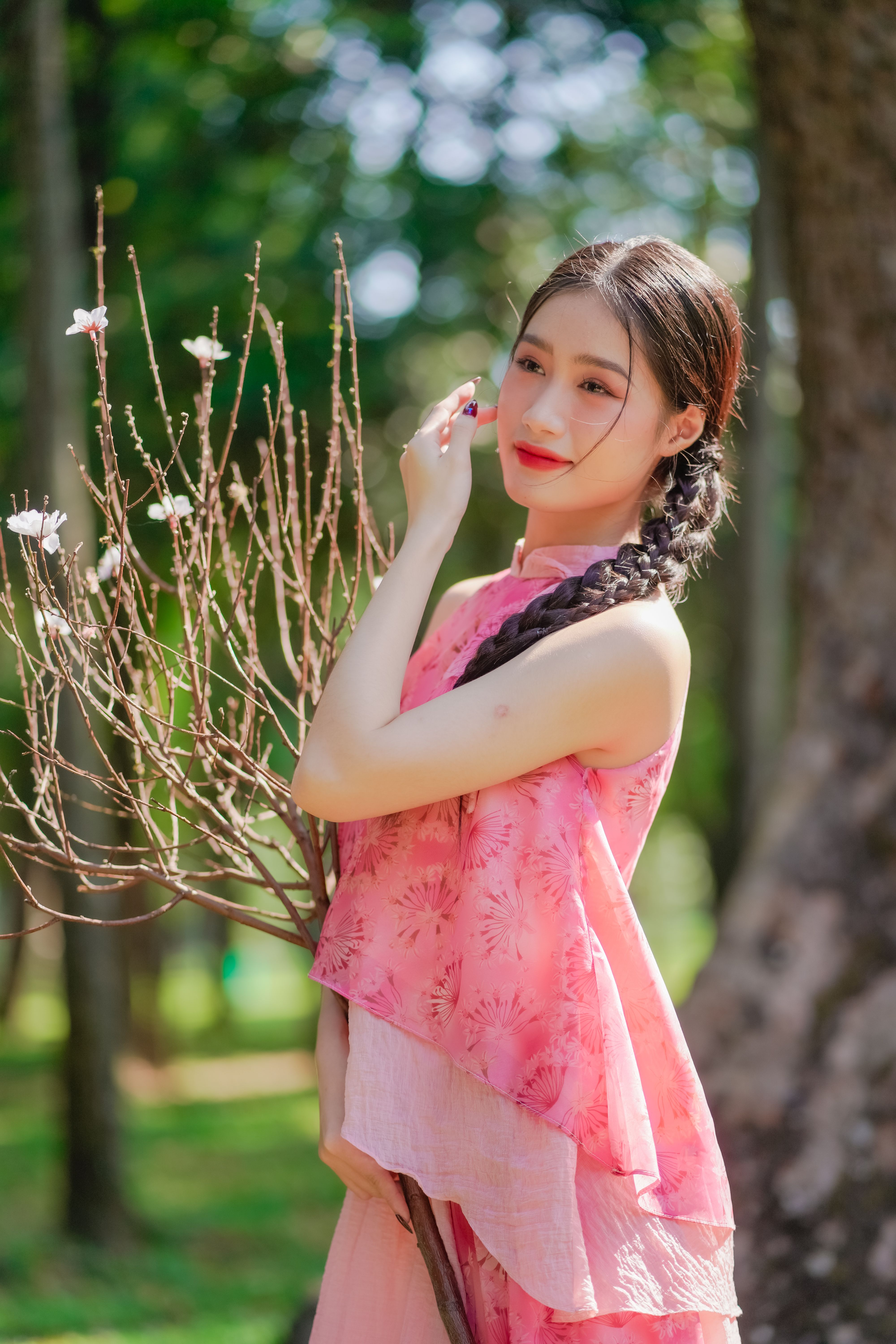 A young woman in a pink dress with braided hair standing outdoors, enjoying nature.