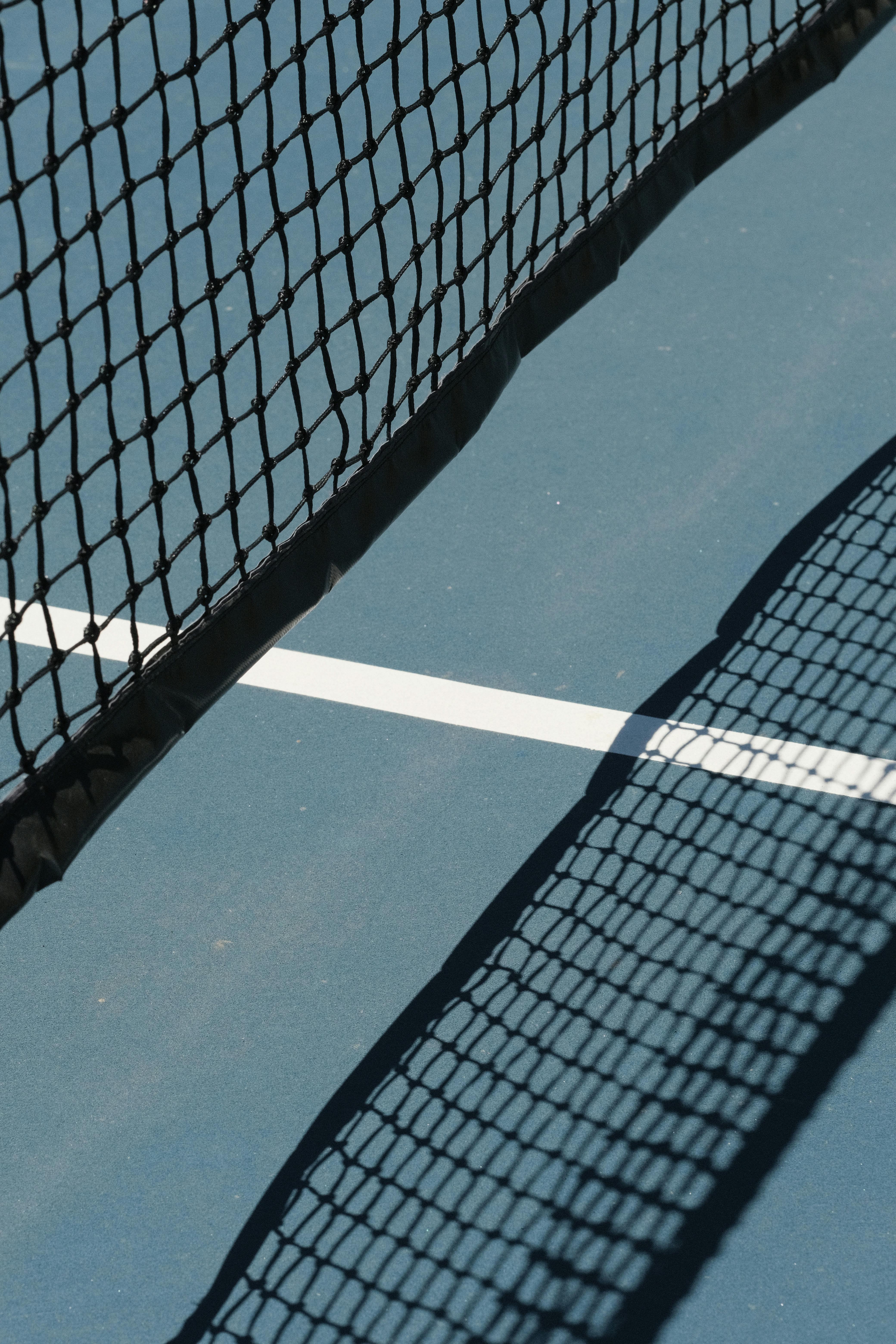 Detailed view of a tennis court net casting a shadow on the blue surface.