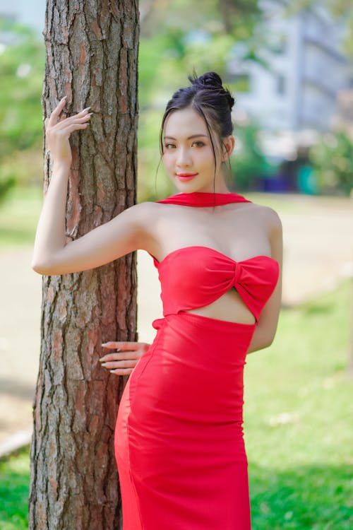 A woman in a red dress posing near a tree
