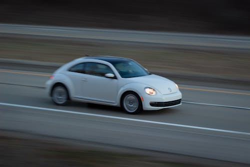A white volkswagen beetle is driving on the road
