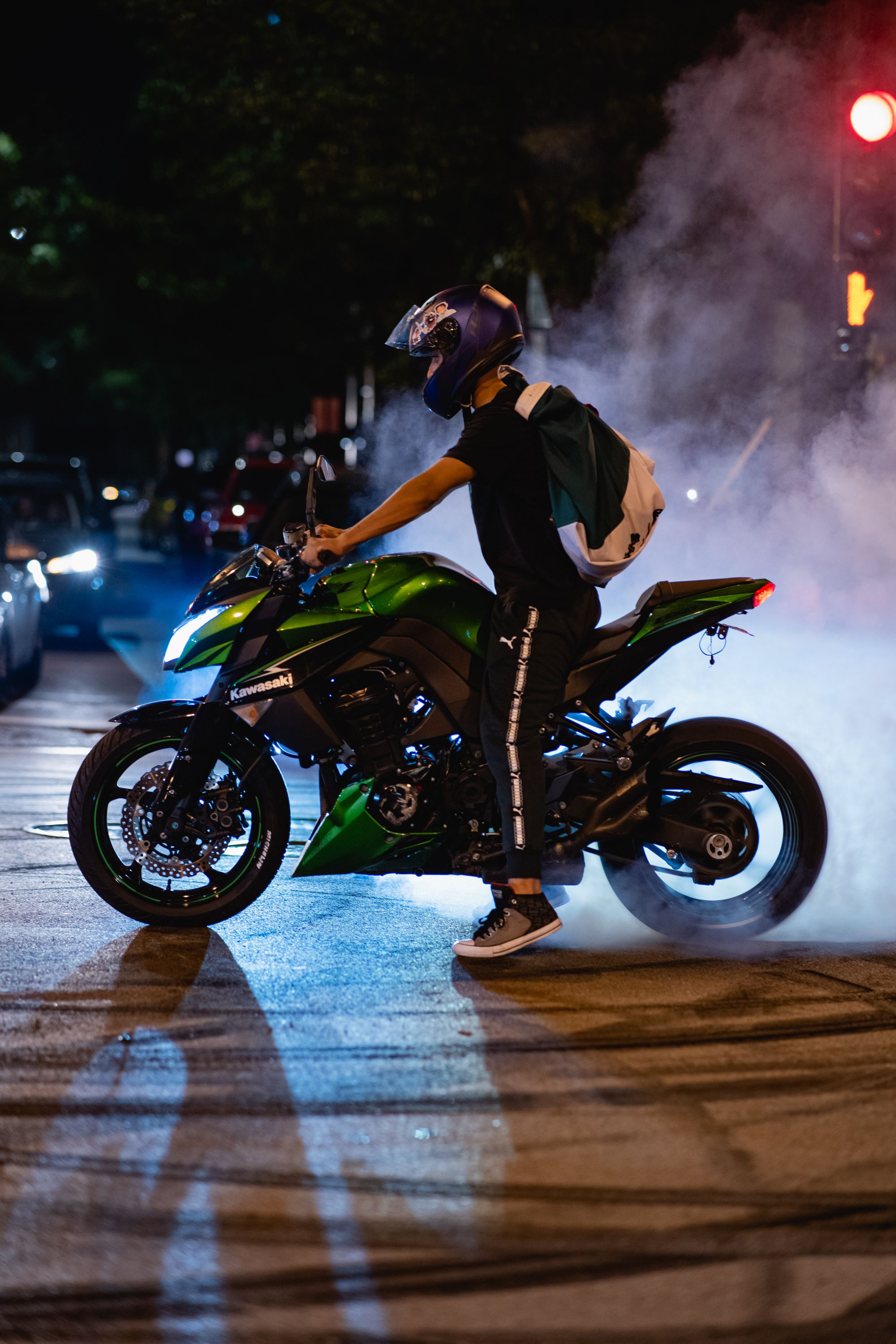 Man riding a motorcycle at night in an urban setting, surrounded by city lights and street smoke.