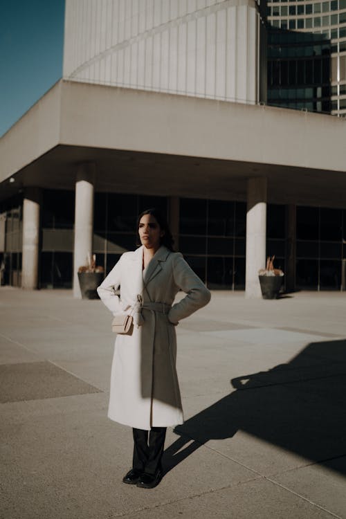 Woman in White Coat on Sunlit Pavement