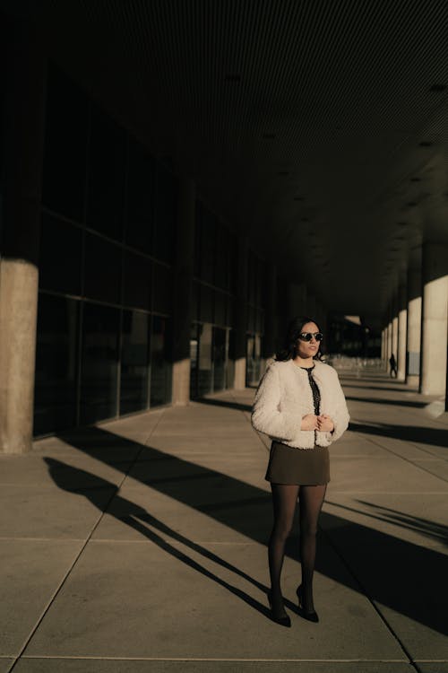 A woman in a black skirt and white jacket standing in an empty building