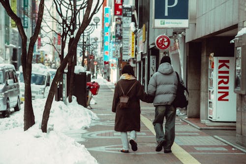 A couple walking down a snowy sidewalk in a city