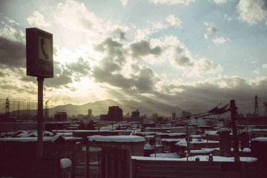 Dramatic winter sunset over an urban landscape in Hokkaido, Japan, with snow-covered rooftops.