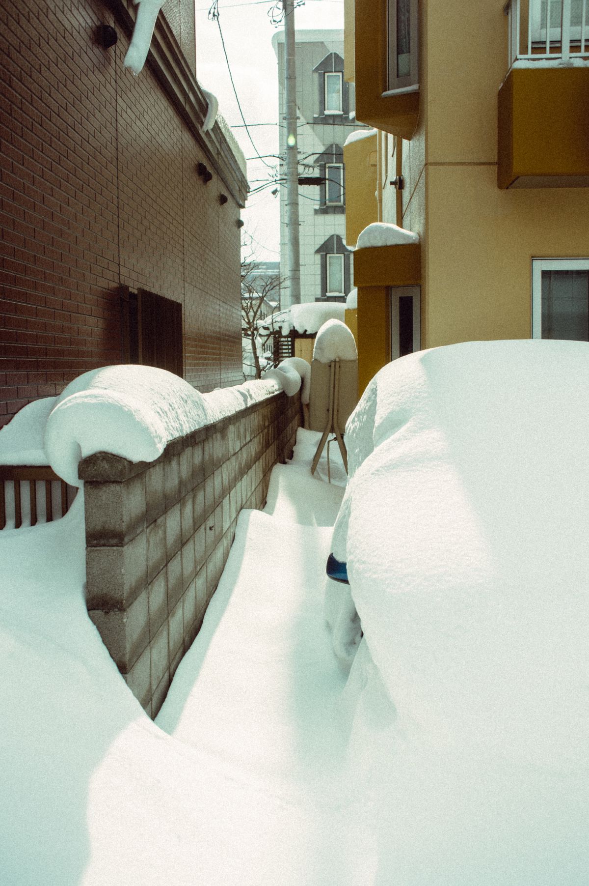 A narrow alley in Hokkaido covered in deep winter snow with urban buildings