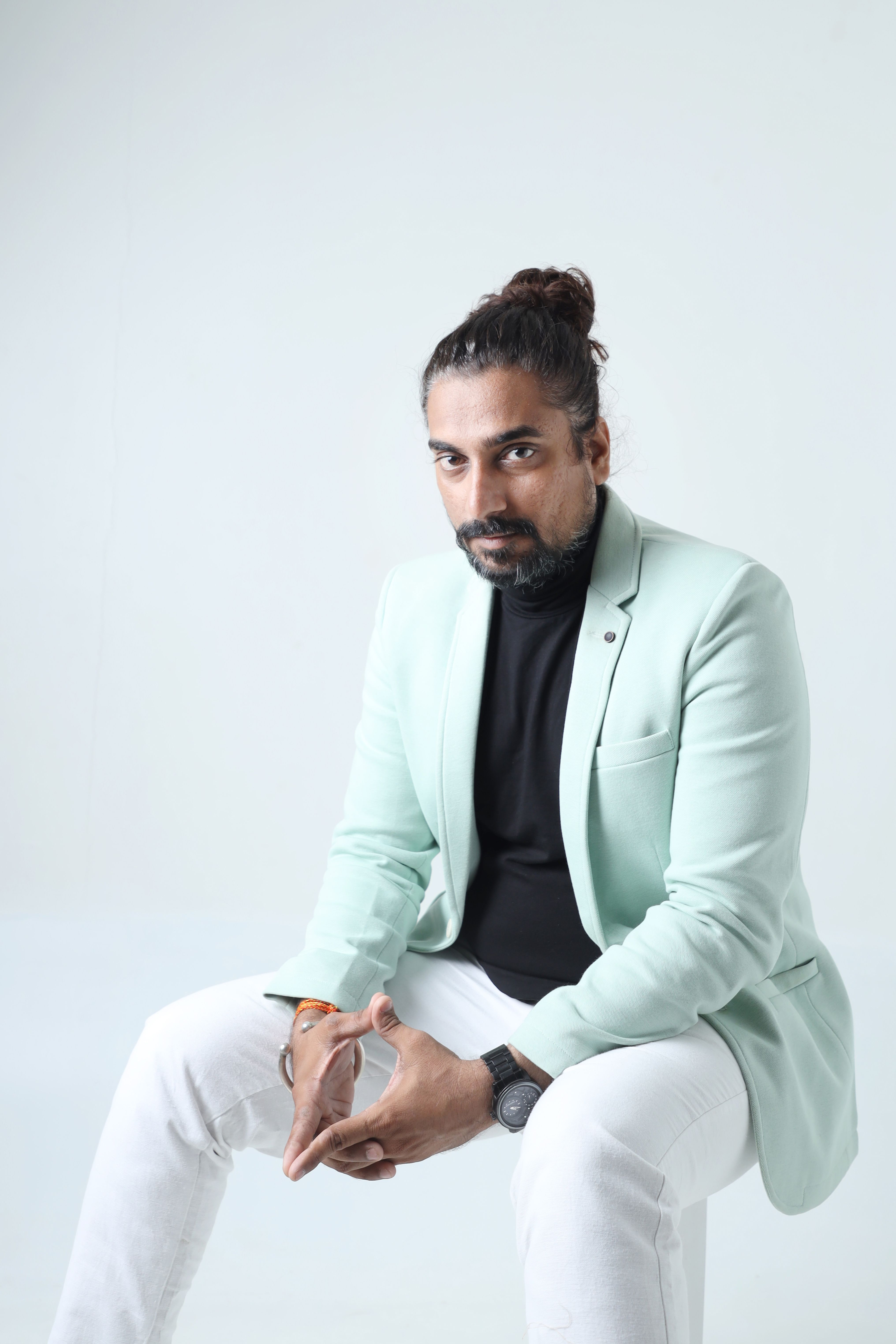 Stylish man with beard and man bun wearing mint blazer posing against minimalistic background.