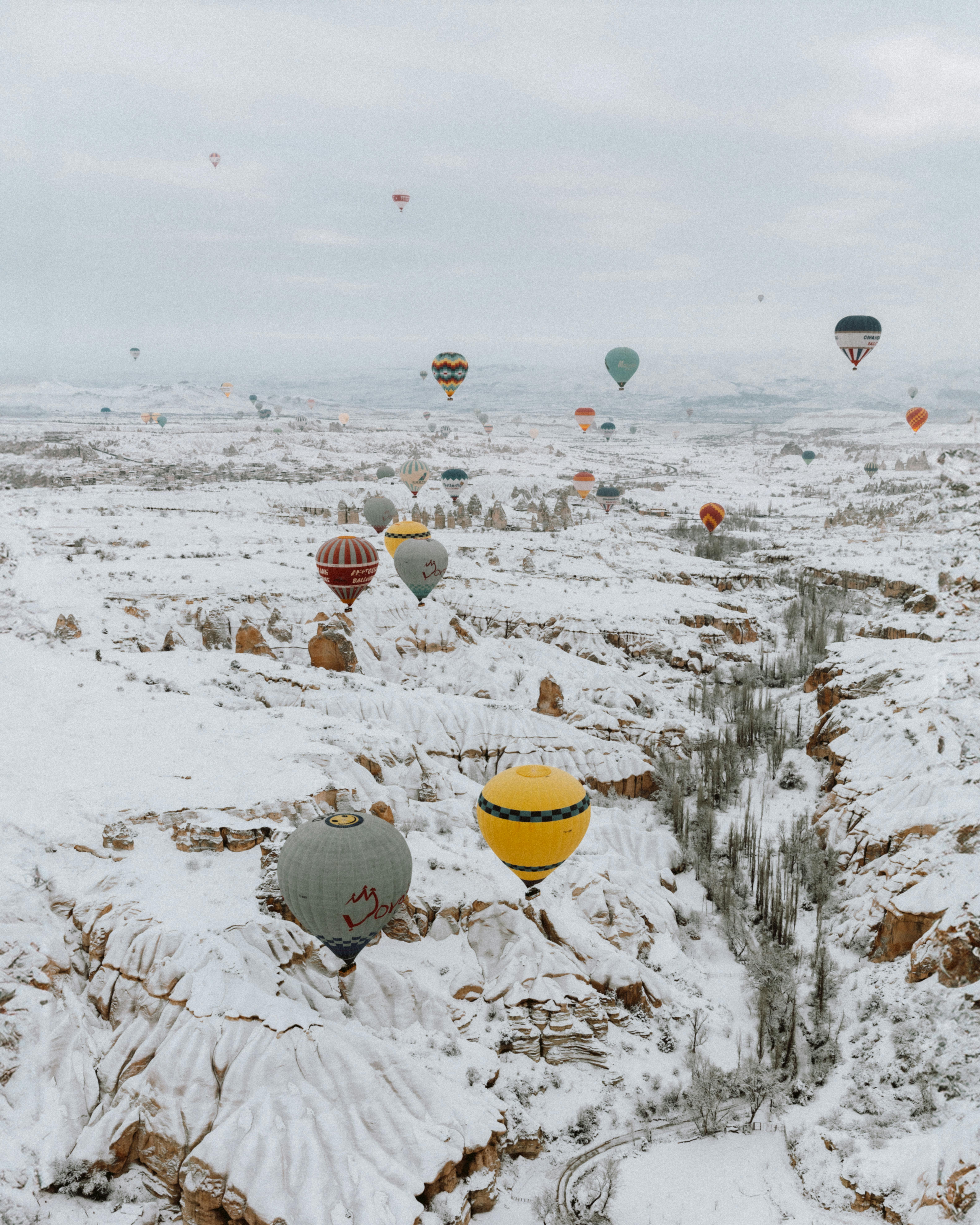 A scenic view of hot air balloons floating over the snow-covered landscape of Cappadocia, Türkiye.