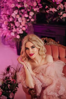 Stylish woman in a pink dress sitting in an ornate chair amidst a floral setting.
