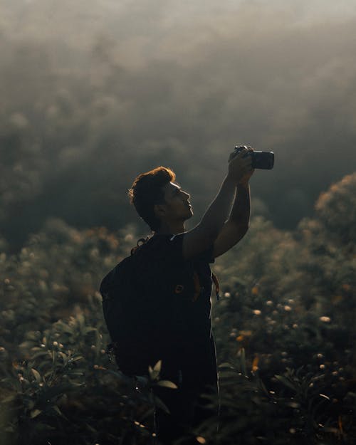 Side View of a Man with a Backpack Taking Pictures with a Camera on a Field 