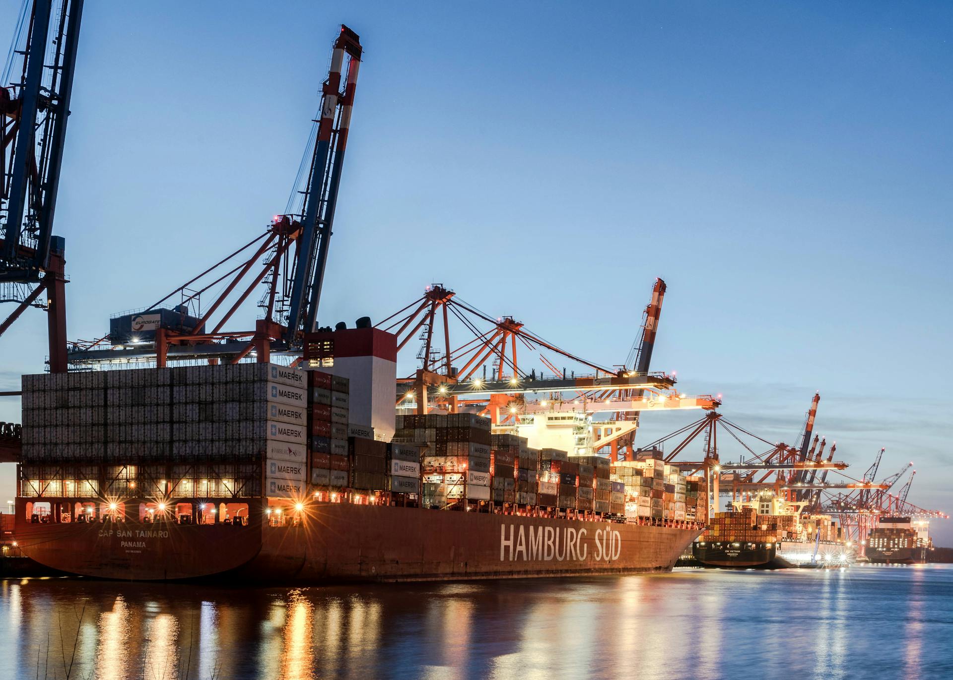 Stunning view of illuminated container ships at Hamburg port with crane operations during twilight.