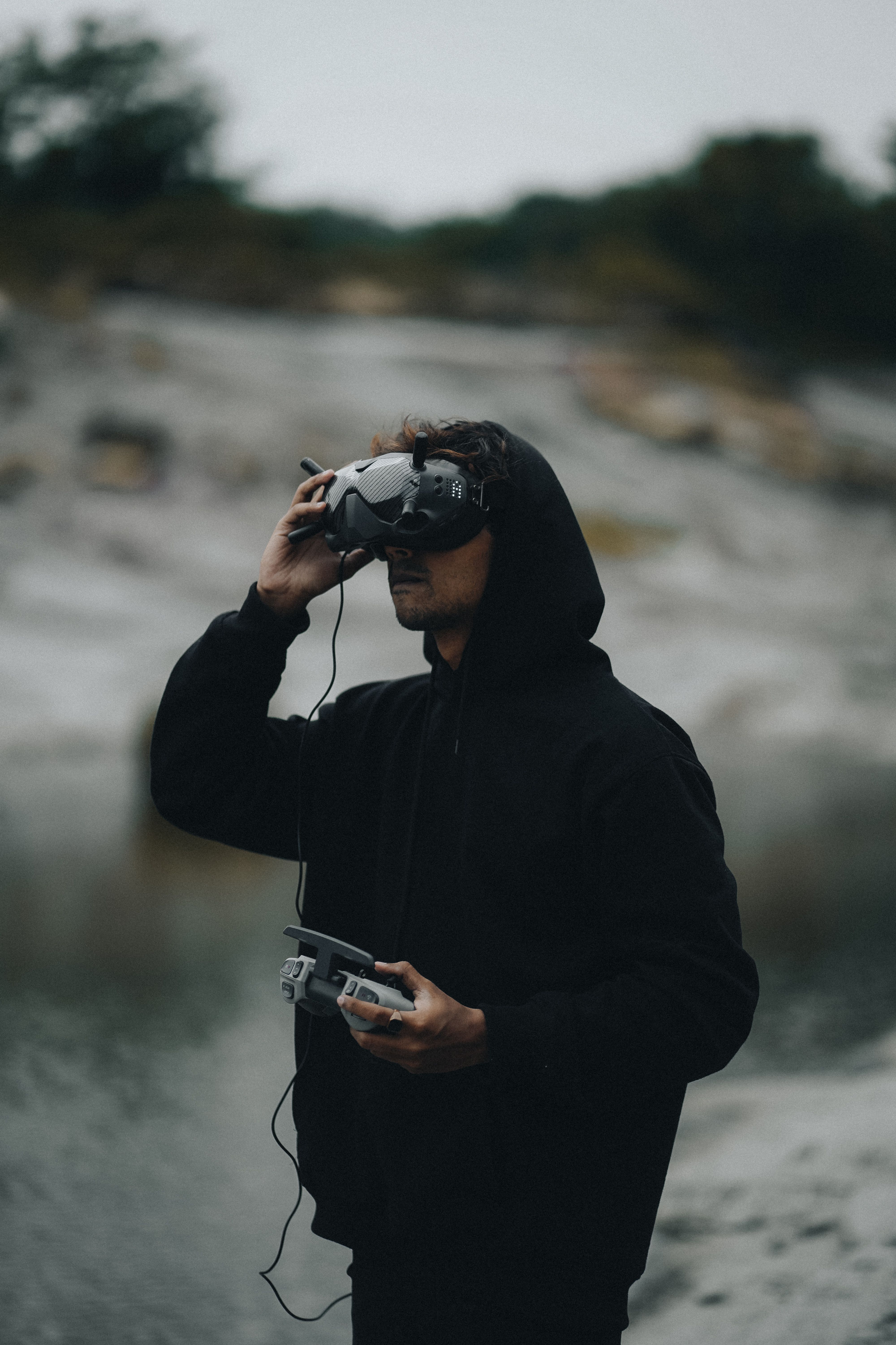 Young man in a hoodie flying a drone using VR goggles, in an outdoor setting.