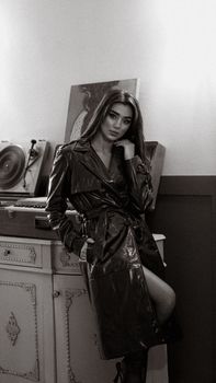 A sophisticated monochrome portrait of a woman posing elegantly in a stylish trench coat indoors.