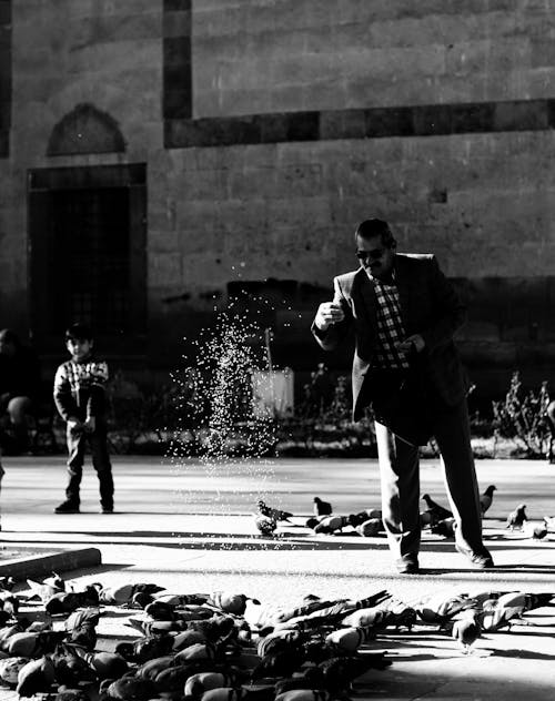 Foto En Escala De Grises Del Hombre A Punto De Dar De Comer A Las Palomas