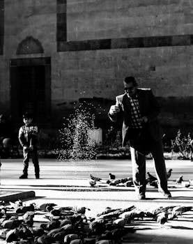 在黑白相间的城市环境中，一名男子和一名男孩正在喂鸽子