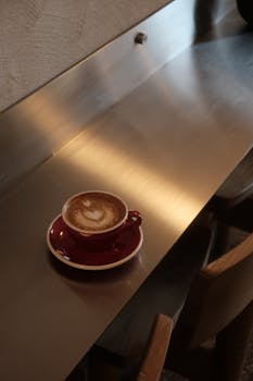 Enjoy a frothy latte served in a red cup on a modern metal countertop for a cozy vibe.