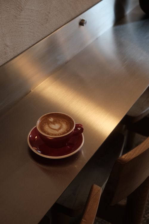 Free Enjoy a frothy latte served in a red cup on a modern metal countertop for a cozy vibe. Stock Photo