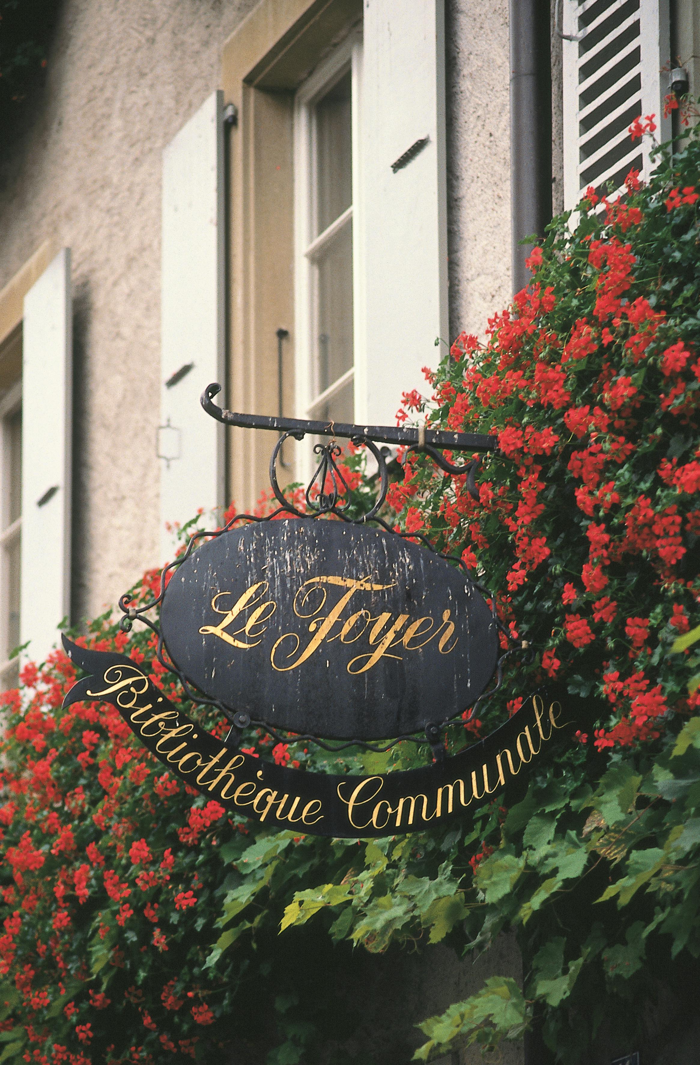 A vintage library sign surrounded by vibrant red flowers in Saint-Prex, Switzerland.