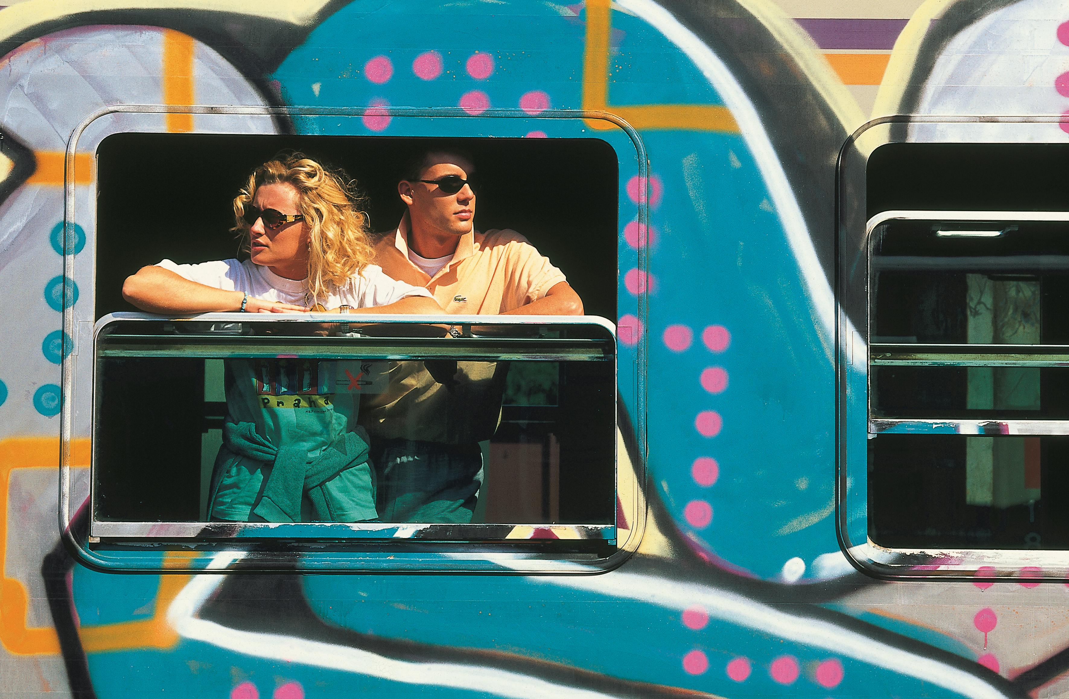 A couple stands at a graffiti-covered train window, enjoying the sunny day in Levico Terme, Italy.