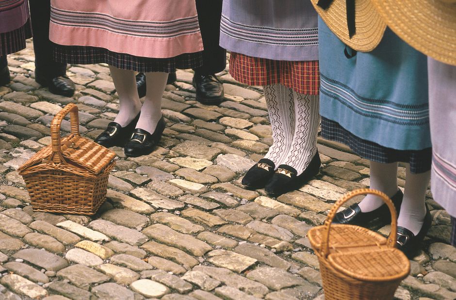 Children in traditional Swiss attire with wicker baskets on cobblestone streets of Nyon, Switzerland.