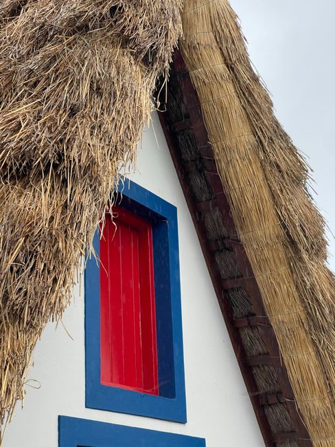 Close-up of a rustic thatched roof house with red and blue accents in Madeira, Portugal.