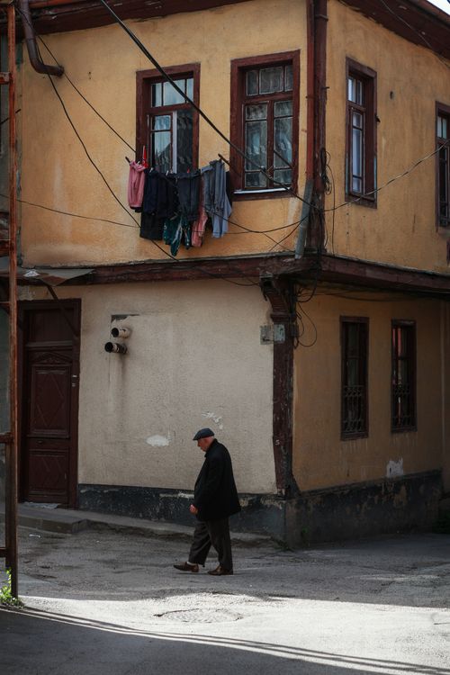 Free Elderly man walks past a rustic urban building with clothesline in a quiet town corner. Stock Photo