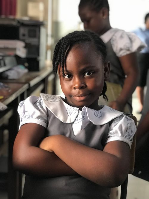 Free Portrait of a smiling schoolgirl confidently posing with arms crossed in a classroom in Ghana. Stock Photo